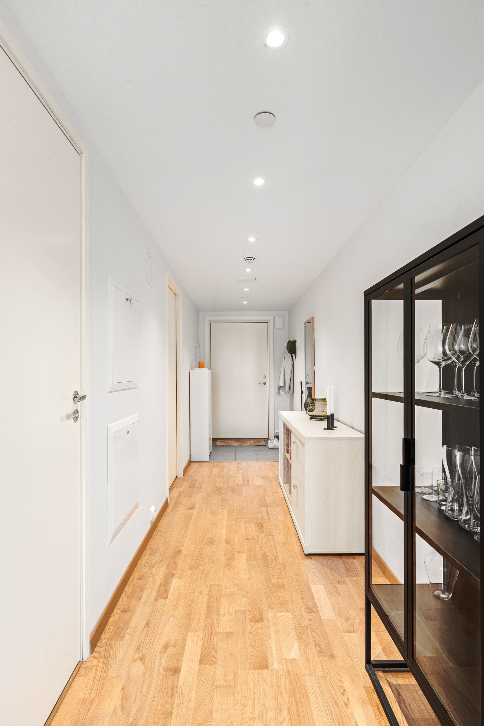 Romslig gang med parkettgulv, lyse vegger og downlights i himling