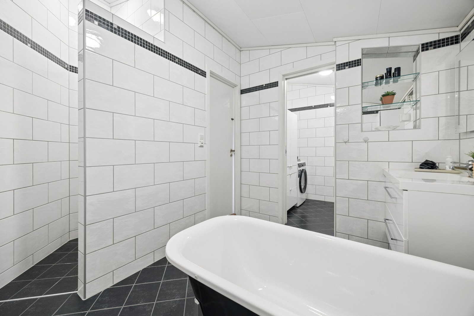 Sammenslått bad og vaskerom innredet med servant, badekar og opplegg for vaskemaskin. Galleribilde