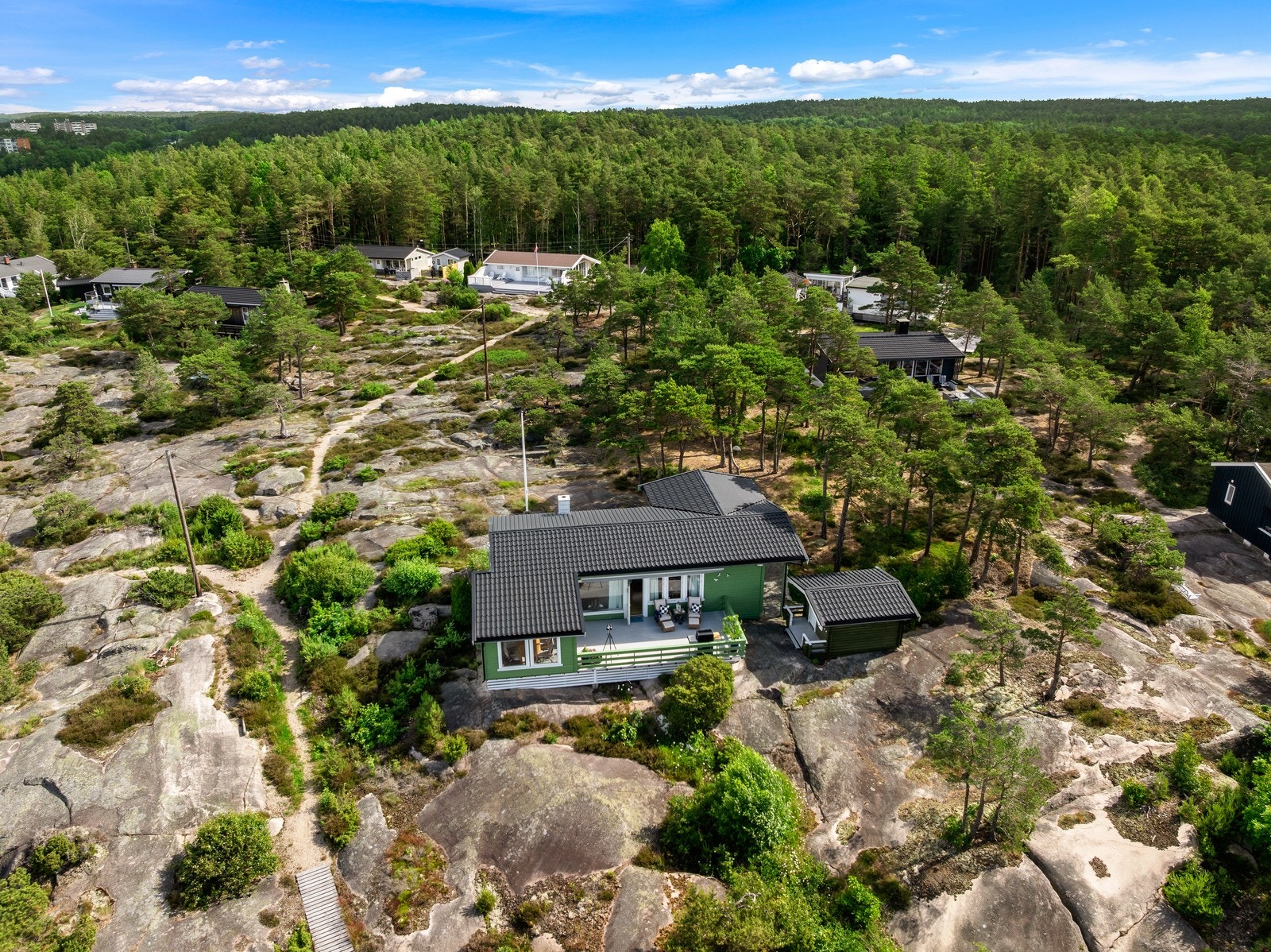 Dronebildet viser eiendommens private og luftige plassering mellom svaberg, furutrær og fritidsbebyggelse. Tilstandsrapporten oppgir totalt 79 m² BRA for alle bygg. Galleribilde