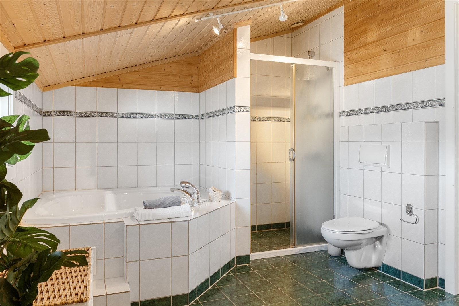 Videre er det veggmontert dusj med skjermvegg/dusjnisje og innfliset boblebad. Galleribilde