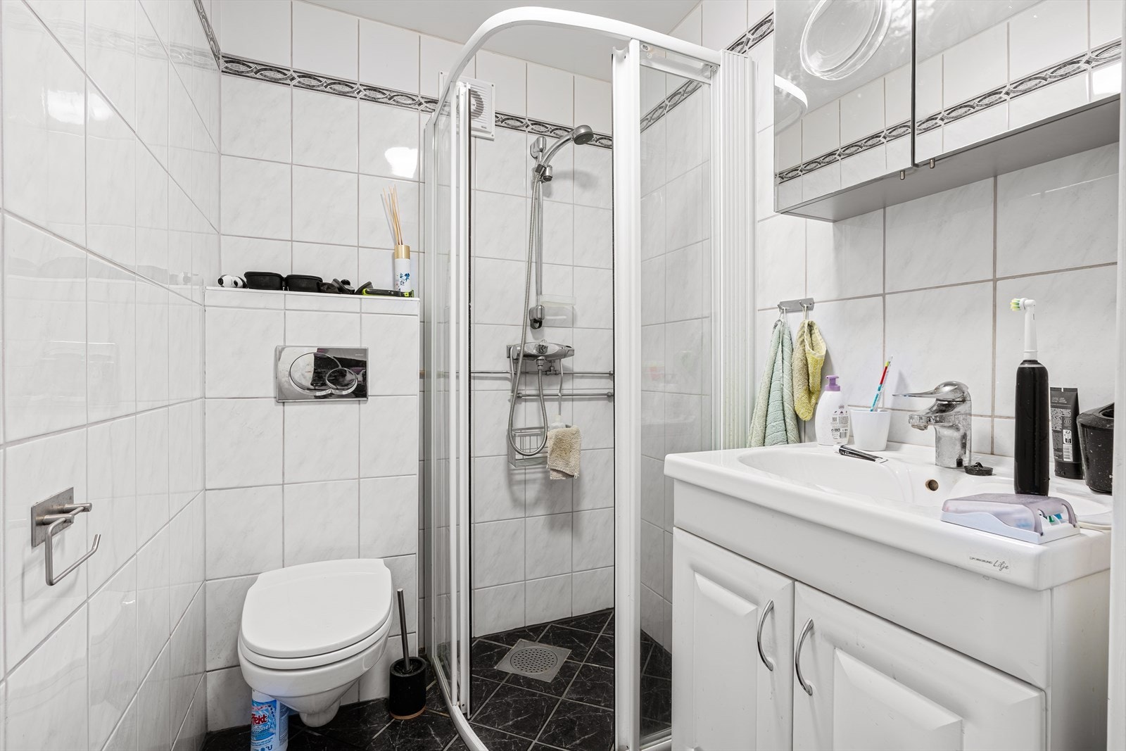 Badet er innredet med vegghengt toalett, dusjhjørne, servant med møblement og speil. Galleribilde