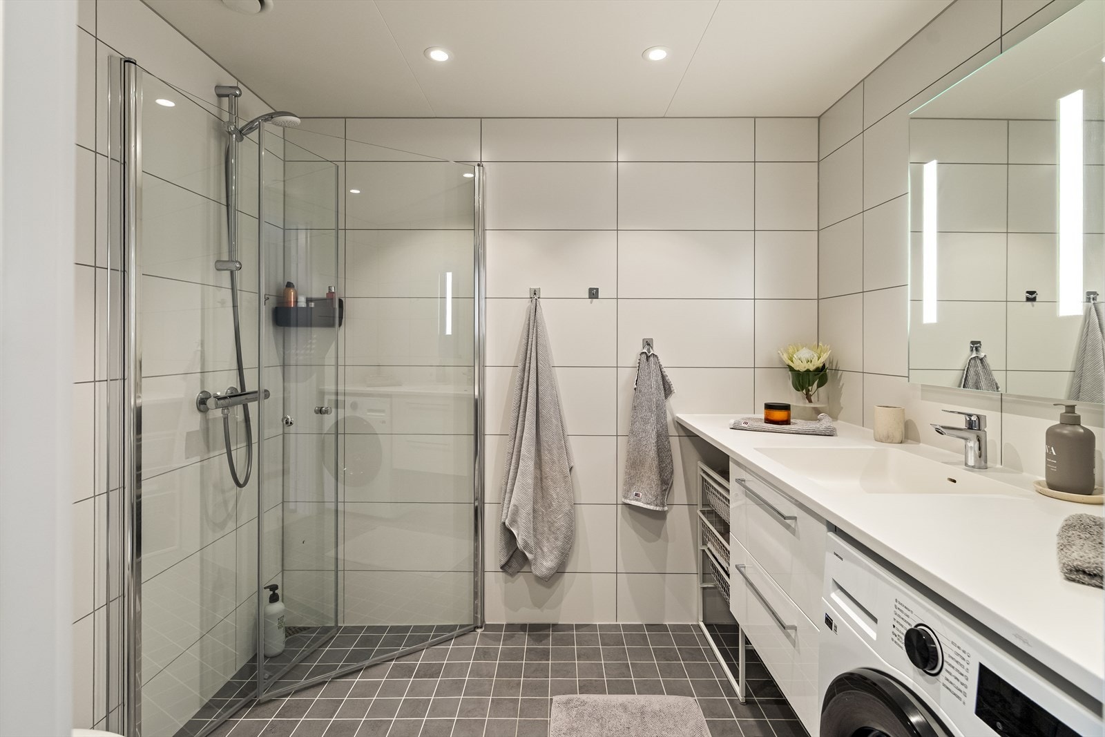 Badet er moderne og helflislagt med tidløse materialvalg. Rommet er innredet med servant i baderomsinnredning, vegghengt toalett og dusjsone med glassvegger. Galleribilde