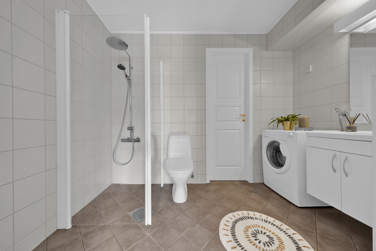 Badet er flislagt i nøytrale farger, har varmekabler i gulv, åpen regnfallsdusj med god plass og praktiske svingdører, samt gjennomgang mellom soverom og disponibelt rom. Galleribilde