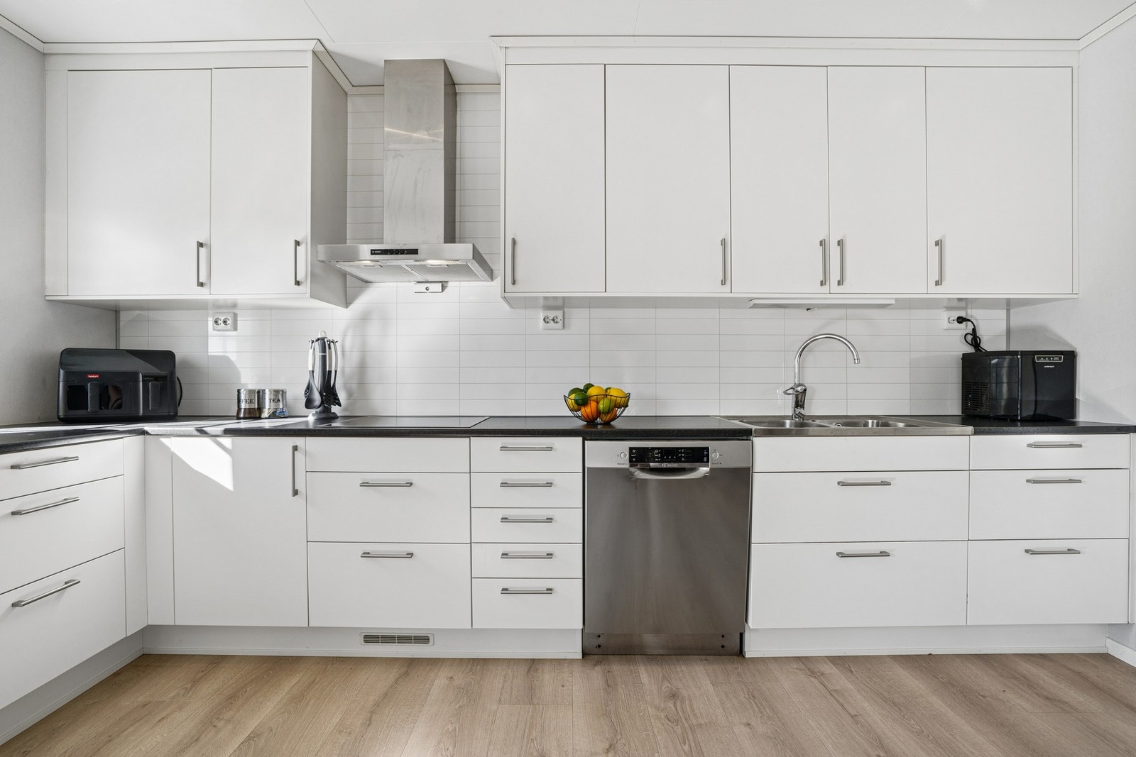 Stilrent og innholdsrikt kjøkken med tidløst design, lyse fronter og mørke benkeplater som skaper en elegant kontrast. Galleribilde