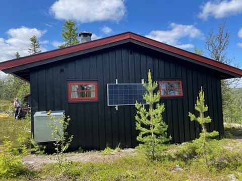 Hytta utvendig sommerstid med gasskasse og solcellepanel (selgers egne bilder) Galleribilde