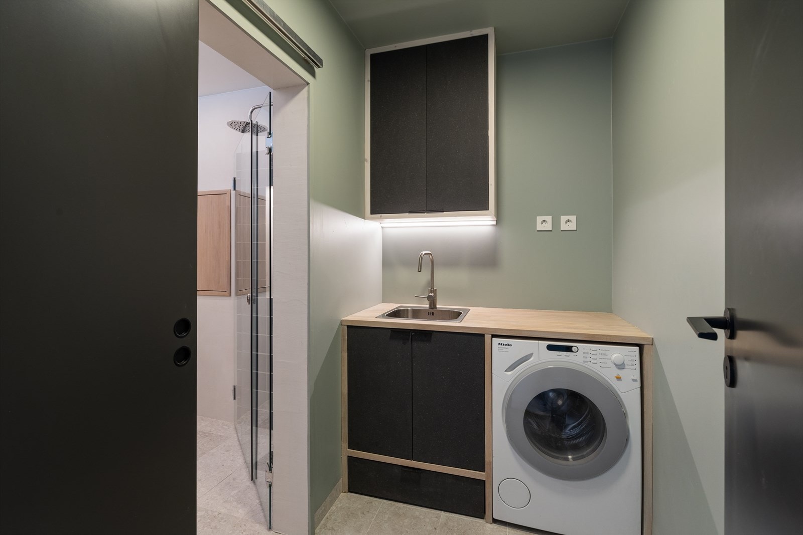 Praktisk vaskeromsdel med plassbygget innredning og medfølgende Miele vaskemaskin. Vaskerommet er adskilt fra badet med en skyvedør. Galleribilde