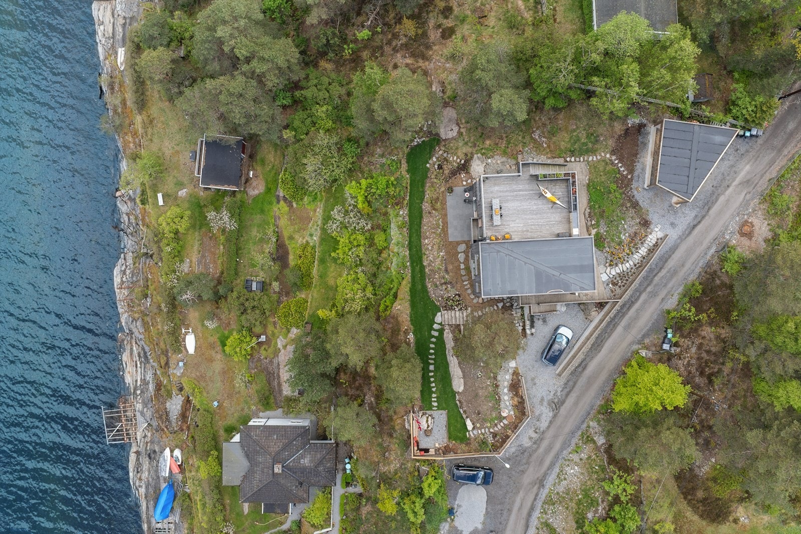 Dronefoto av eiendommen. Parkeringsplass for to biler foran inngang til underetasjen er utstyrt med elbil-lader. Carporten har god plass til to biler. Også den er utstyrt med lader. Galleribilde