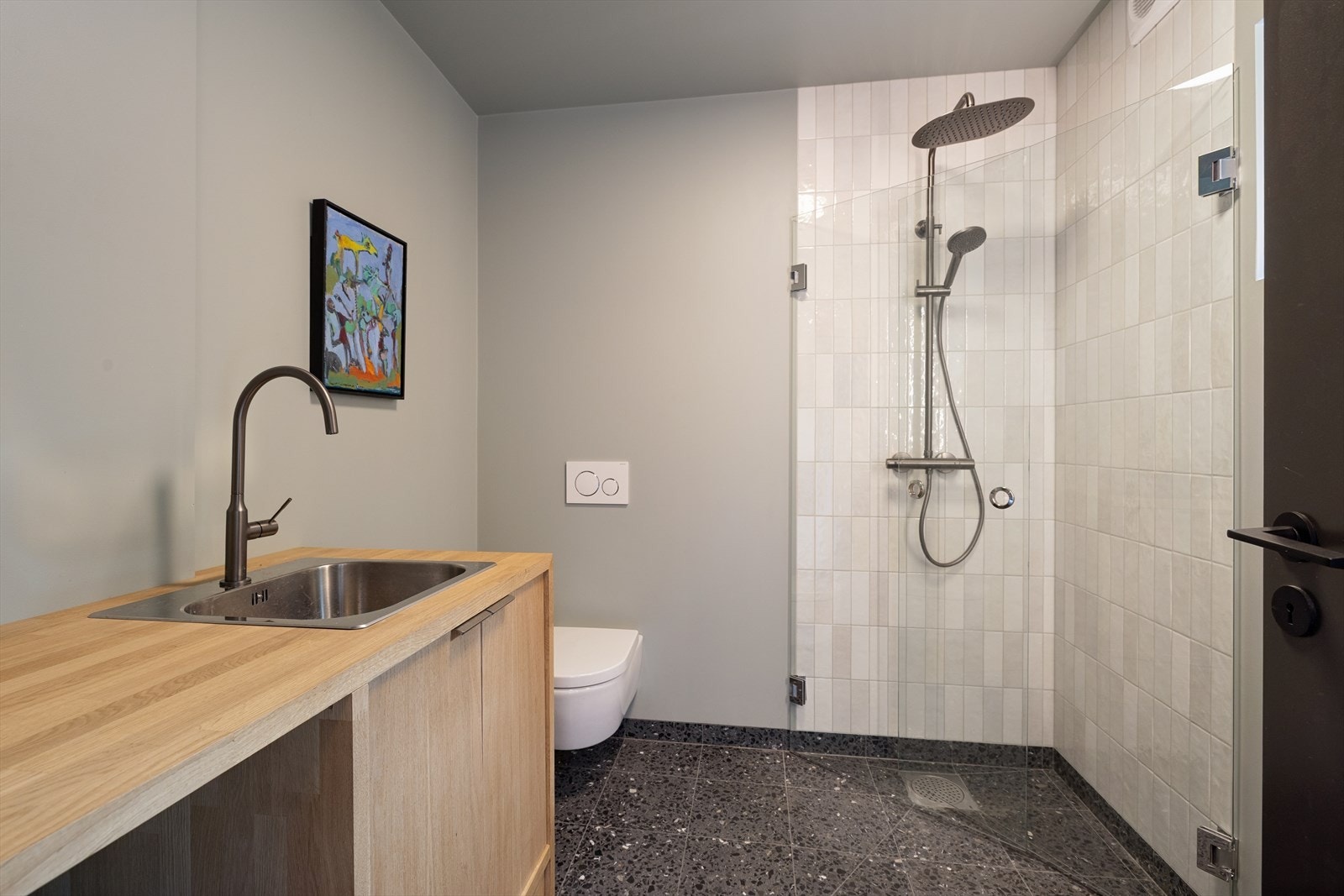 Badet i inngangspartiet er kombinert med vaskerom. Det er terrazzo på gulvet og våtromsmalte vegger i kombinasjon med fliser. Galleribilde