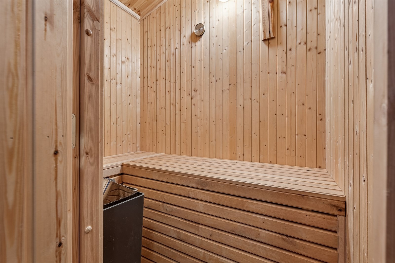 Badstue med panelte vegger og sittebenker i tre, utstyrt med elektrisk badstueovn. Galleribilde