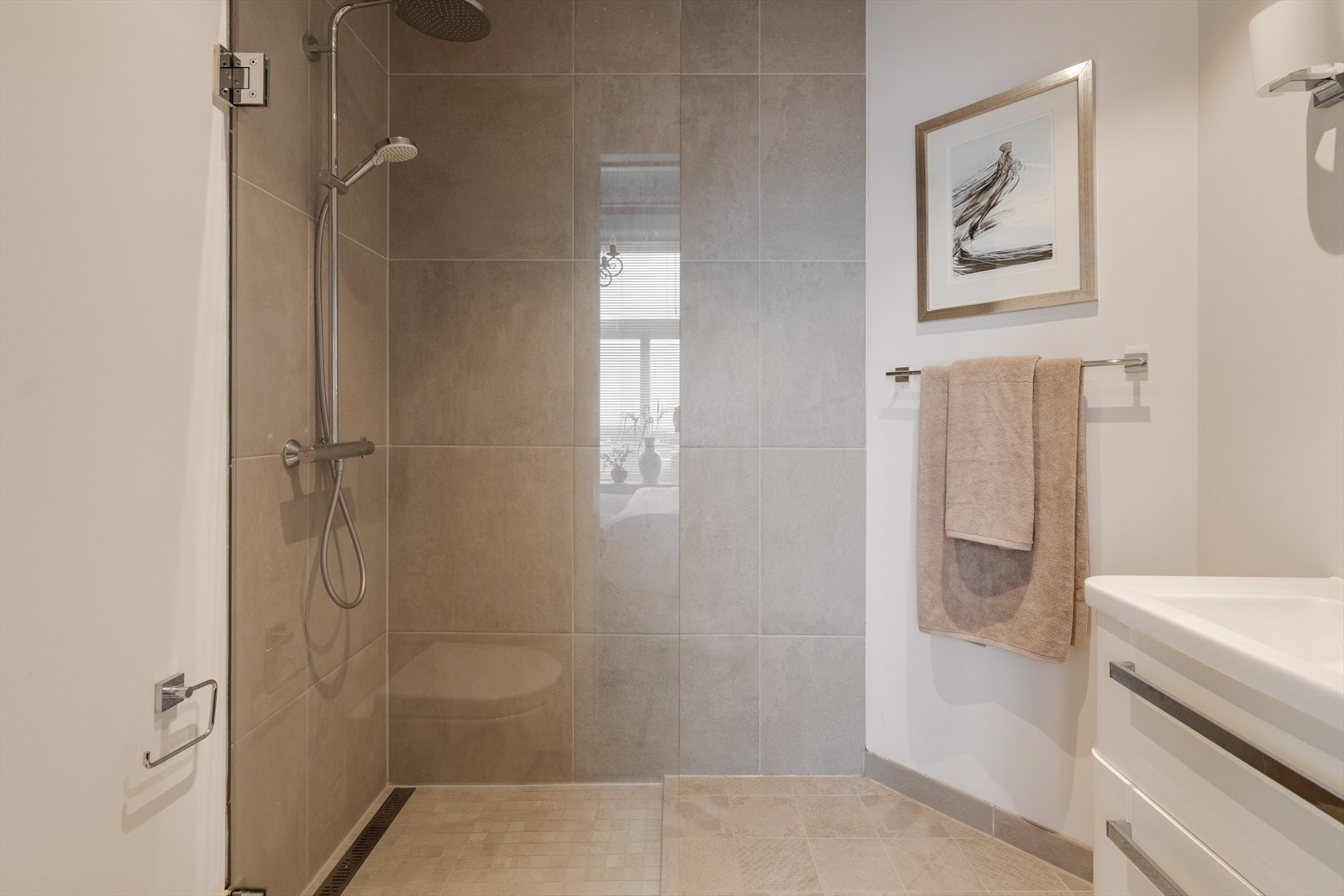 Delikat bad fra 2017 med harmonisk fargepalett i beige og hvite toner, som sammen med downlights i himlingen skaper en lun og innbydende atmosfære. Galleribilde