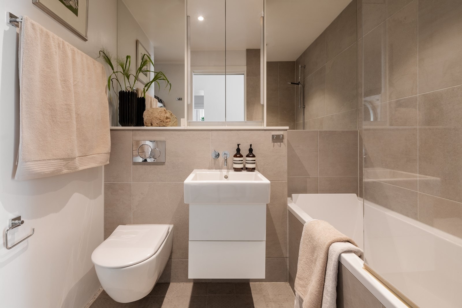 Hovedbadet (2017) og fremstår moderne og funksjonelt med tidløse materialvalg. Badet er innredet i elegante beige og hvite toner, og downlights i taket gir en behagelig belysning. Flislagte gulv med varmekabler sørger for god komfort året rundt. Galleribilde