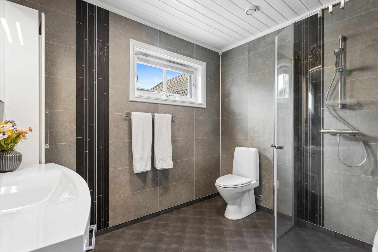 Badet er innredet med romslig dusjssone med glassvegger, stilren baderomsinnredning med god oppbevaringsplass samt vegghengt speil. Galleribilde