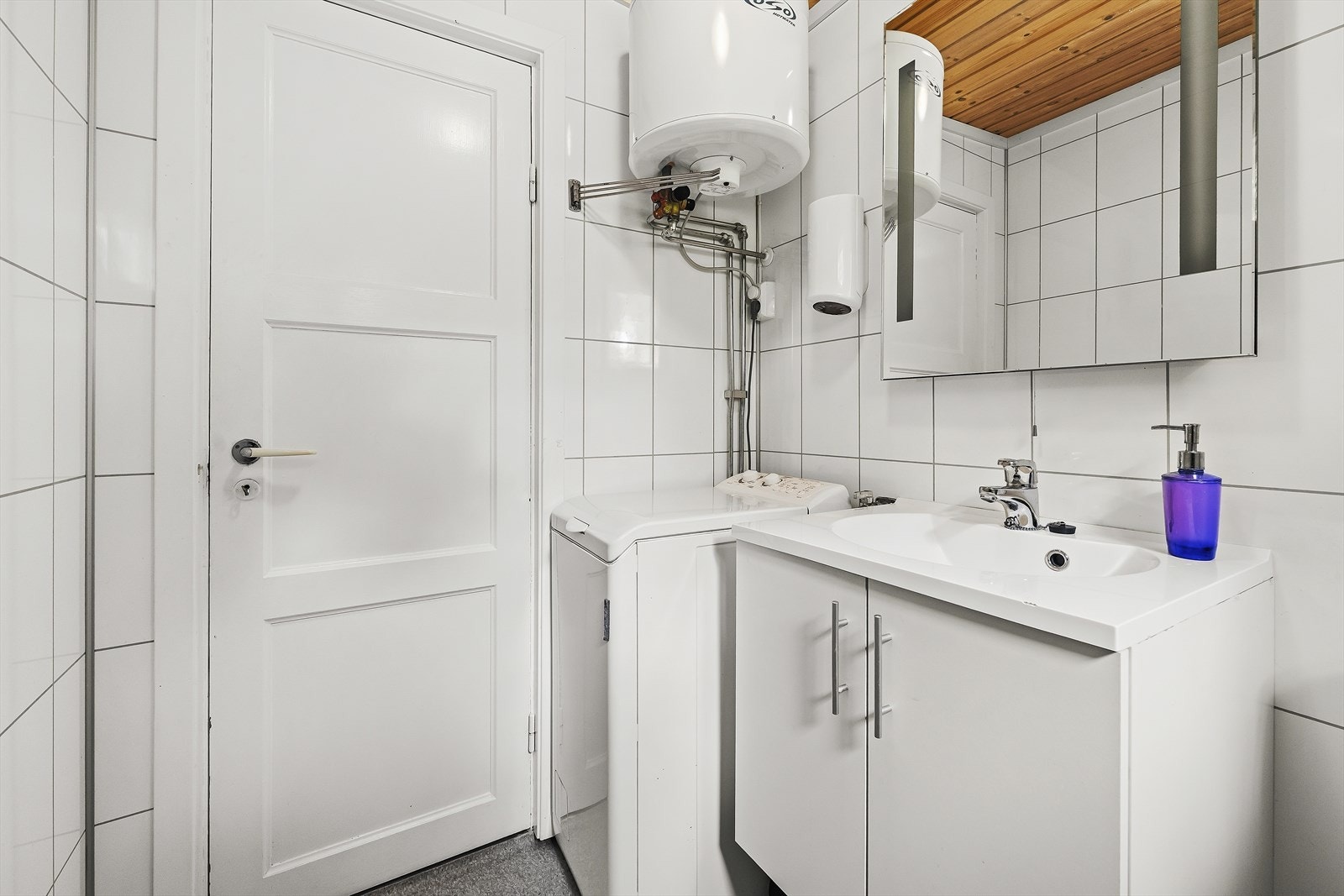 Badet er utstyrt med servant over skapinnredning, speil og toalett. Opplegg til vaskemaskin Galleribilde
