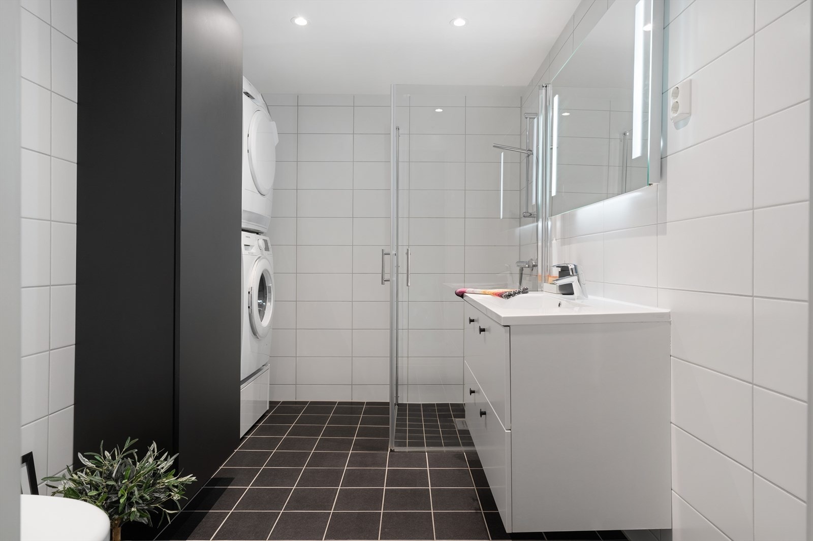 Romslig, flislagt bad på 6 m². Badet inneholder wc, servant med speil, dusj med innfellbare glassdører samt opplegg for vaskemaskin og tørketrommel. Galleribilde