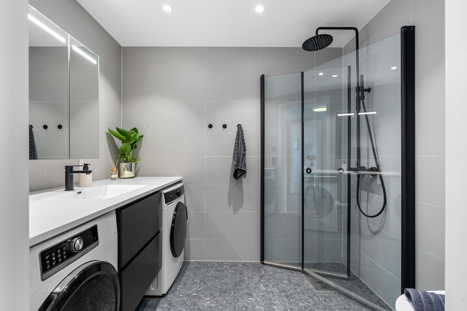 Pent og moderne bad fra byggeår med flislagte overflater og varmekabler i gulv. Badet er innredet med heldekkende servant på underskap, speil, belysning, vegghengt wc og dusj med dusjvegger i herdet glass. Galleribilde