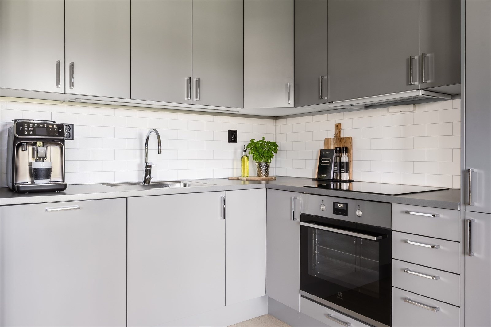 Innredningen har grå glatte fronter og laminert benkeplate med planlimt oppvaskkum. Både fint og praktisk med lyse fliser i benkeryggen og belysning under overskapene. Galleribilde