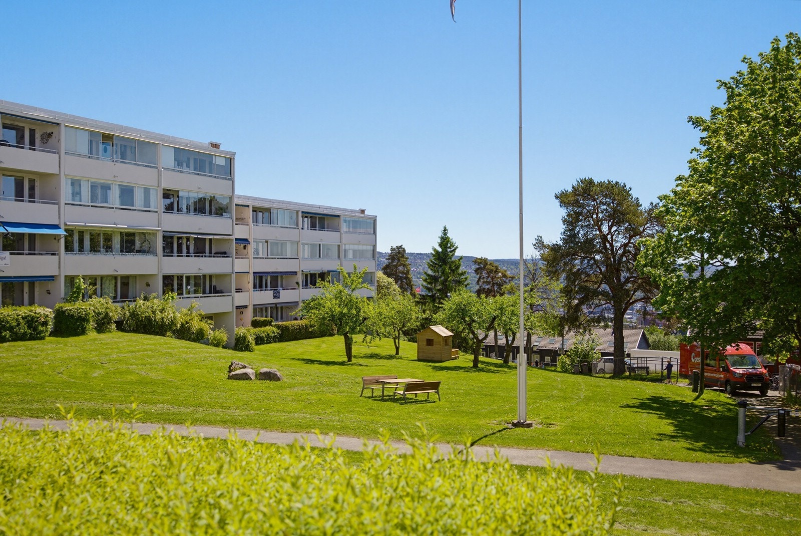 Store, parkmessige fellesarealer med sittegrupper og lekeapparater. Galleribilde