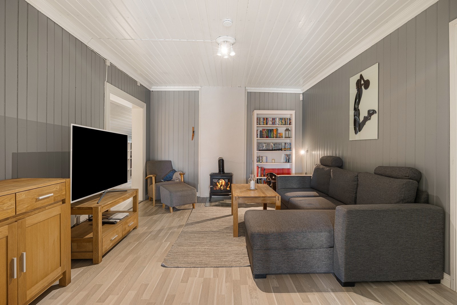 Stuen er innredet med peisovn, laminatgulv og gråmalte panelvegger. Galleribilde