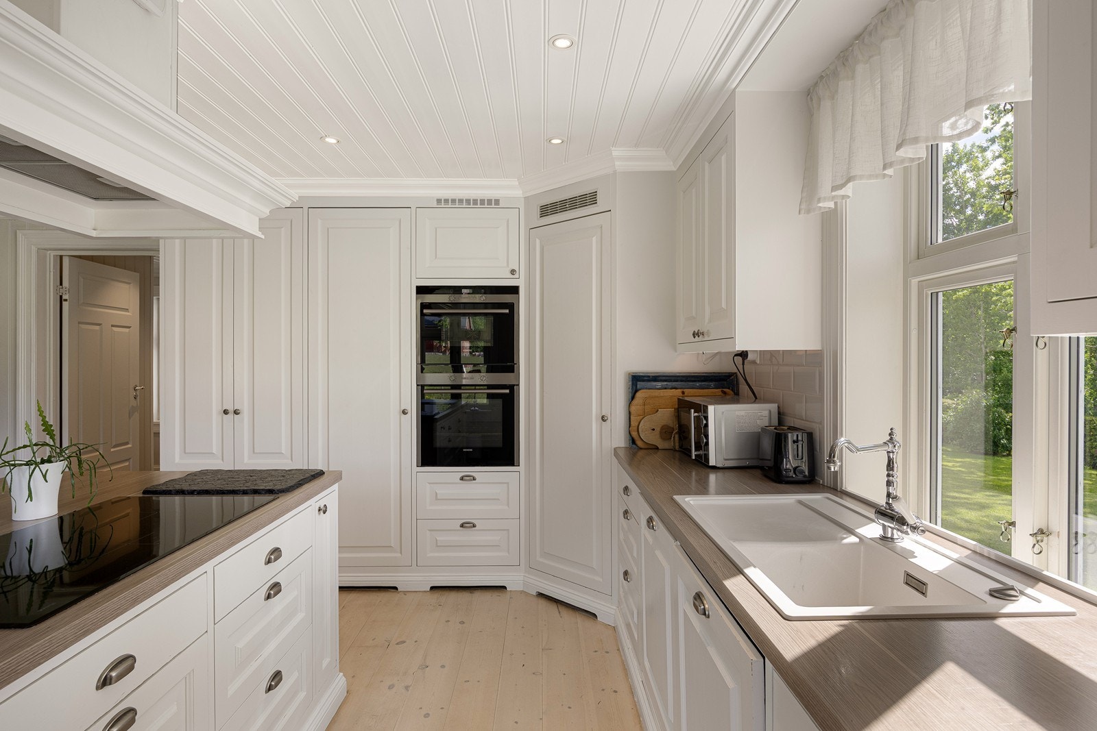 Kjøkkeninredningen er fra 2012, med hvite, profilerte heltrefronter, benkeplate av laminat, elegant armatur og nedfelt oppvaskkum i hvitt design. Galleribilde