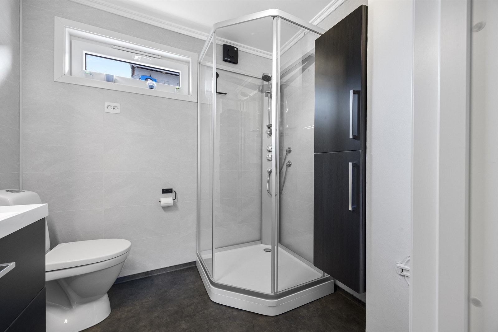 Badet er utstyrt med dusjkabinett, vegghengt toalett og servant med skuffeseksjon. Galleribilde