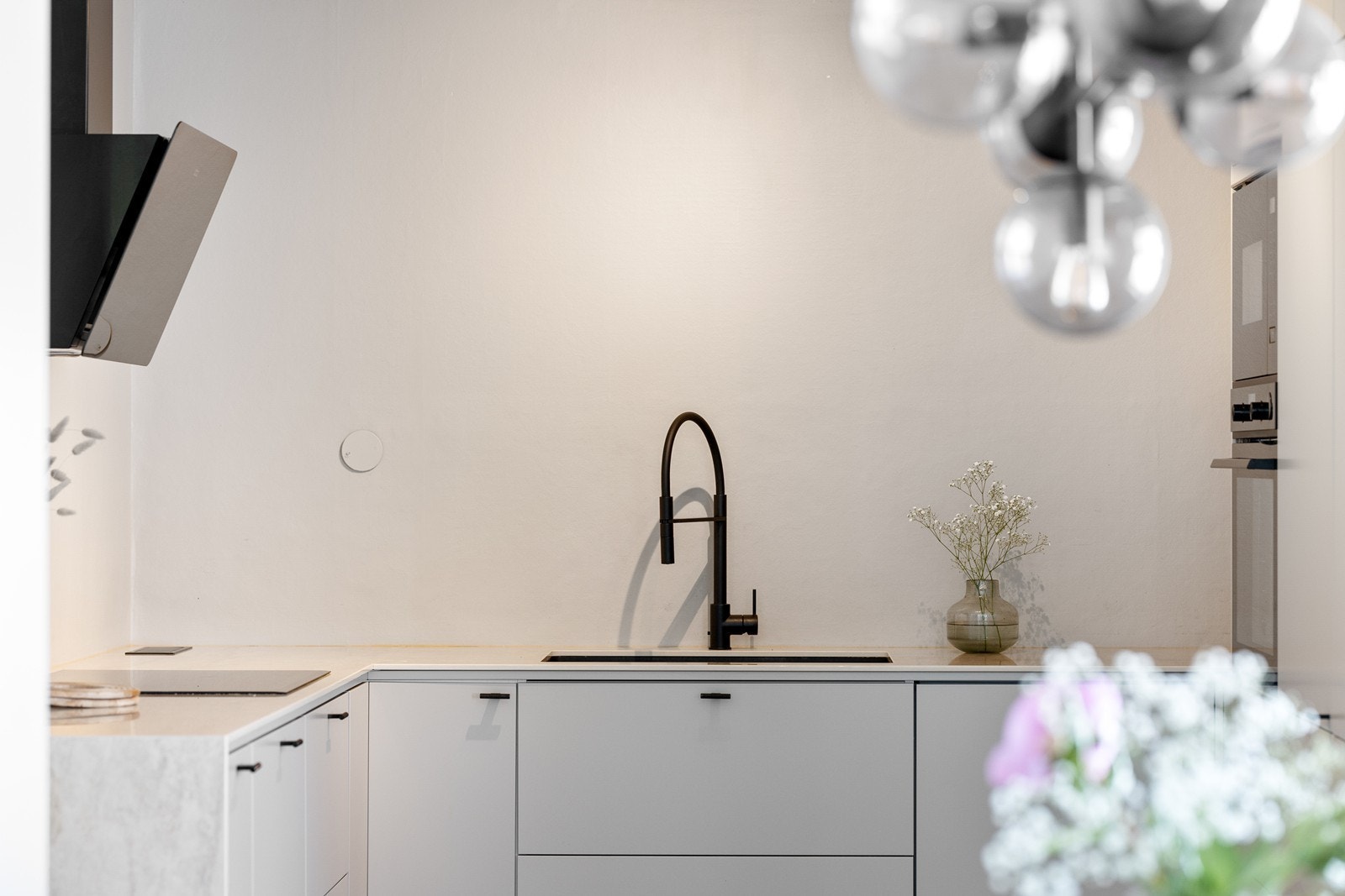 Kjøkkenet fremstår som svært minimalistisk og elegant med slette, lyse fronter, grep i sort utførelse og en delikat steinbenkeplate i marmor. Galleribilde