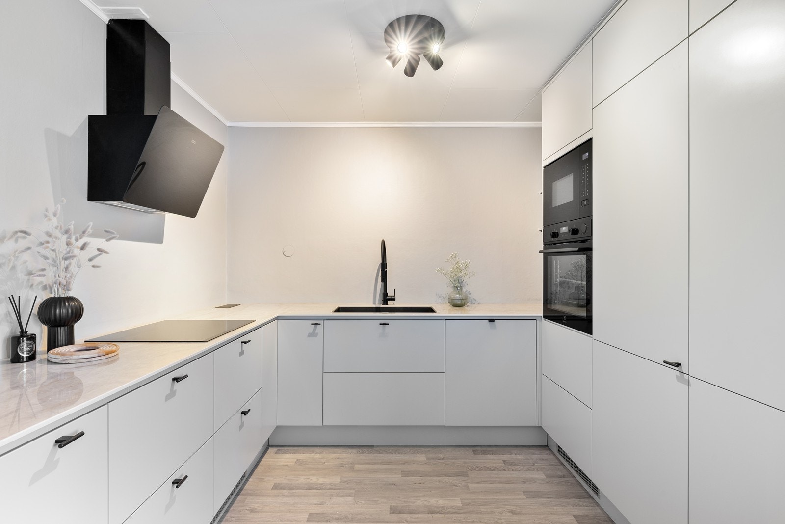 Det er lagt stor vekt på moderne design og funksjonalitet, noe som understrekes av den stilfulle, sorte kjøkkenkranen og en matchende, skråstilt sort ventilator over induksjonstoppen. Galleribilde