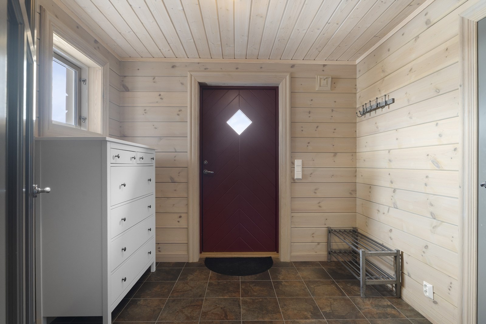 Romslig entré med flislagt gulv. Trepanel på vegger og i himling viderefører materialspråket fra fasaden. Det er god plass til å henge fra seg yttertøy. Galleribilde