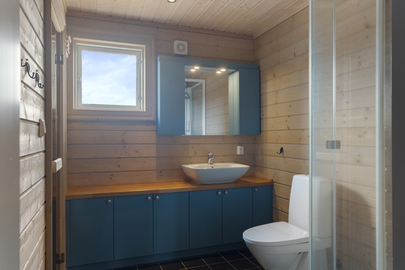 Badet i hovedetasjen har dusjkabinett, toalett og innredning med vask. Vegger og himling har overflater av trepanel, og baderomsgulvet er flislagt. Galleribilde