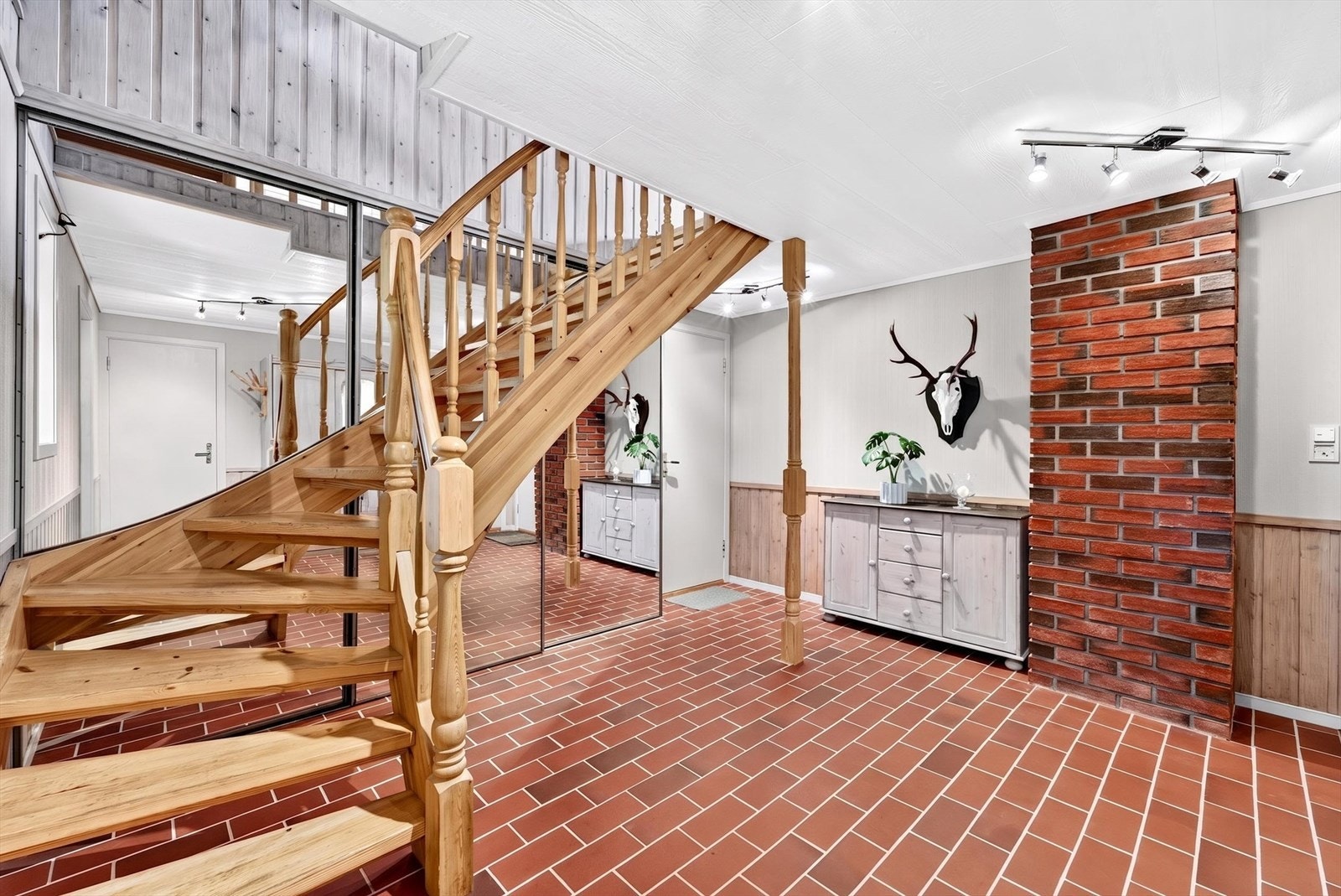 Romslig hall med trapp i tre som forbinder boligens tre etasjer. Galleribilde