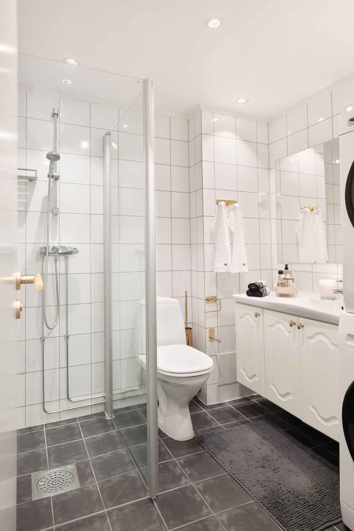 Badet er innredet med servantseksjon med skap, speil over servant, dusjhjørne med inn-/utadslående dører i herdet glass og gulvmontert toalett. Galleribilde