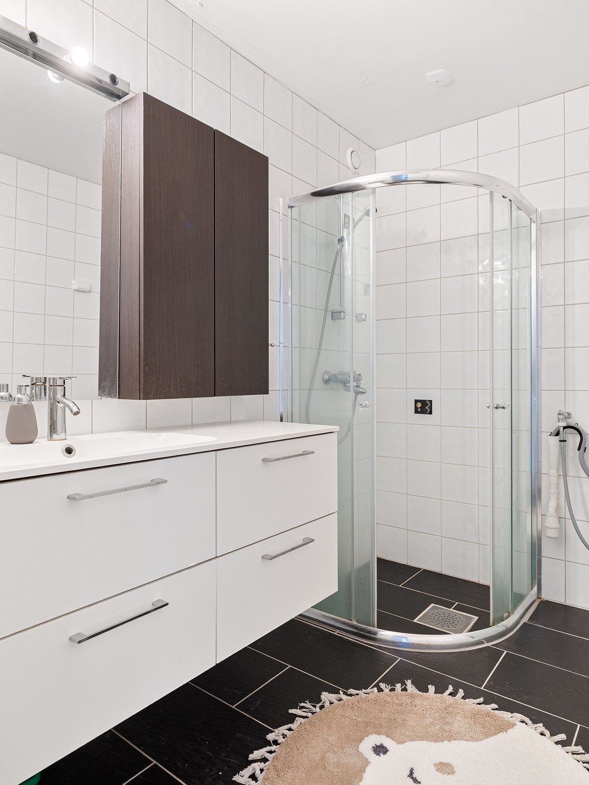 Rommet er innredet med en romslig baderomsinnredning med mye oppbevaringsplass. Videre er badet utstyrt med dusjhjørne og opplegg for vaskemaskin. Galleribilde