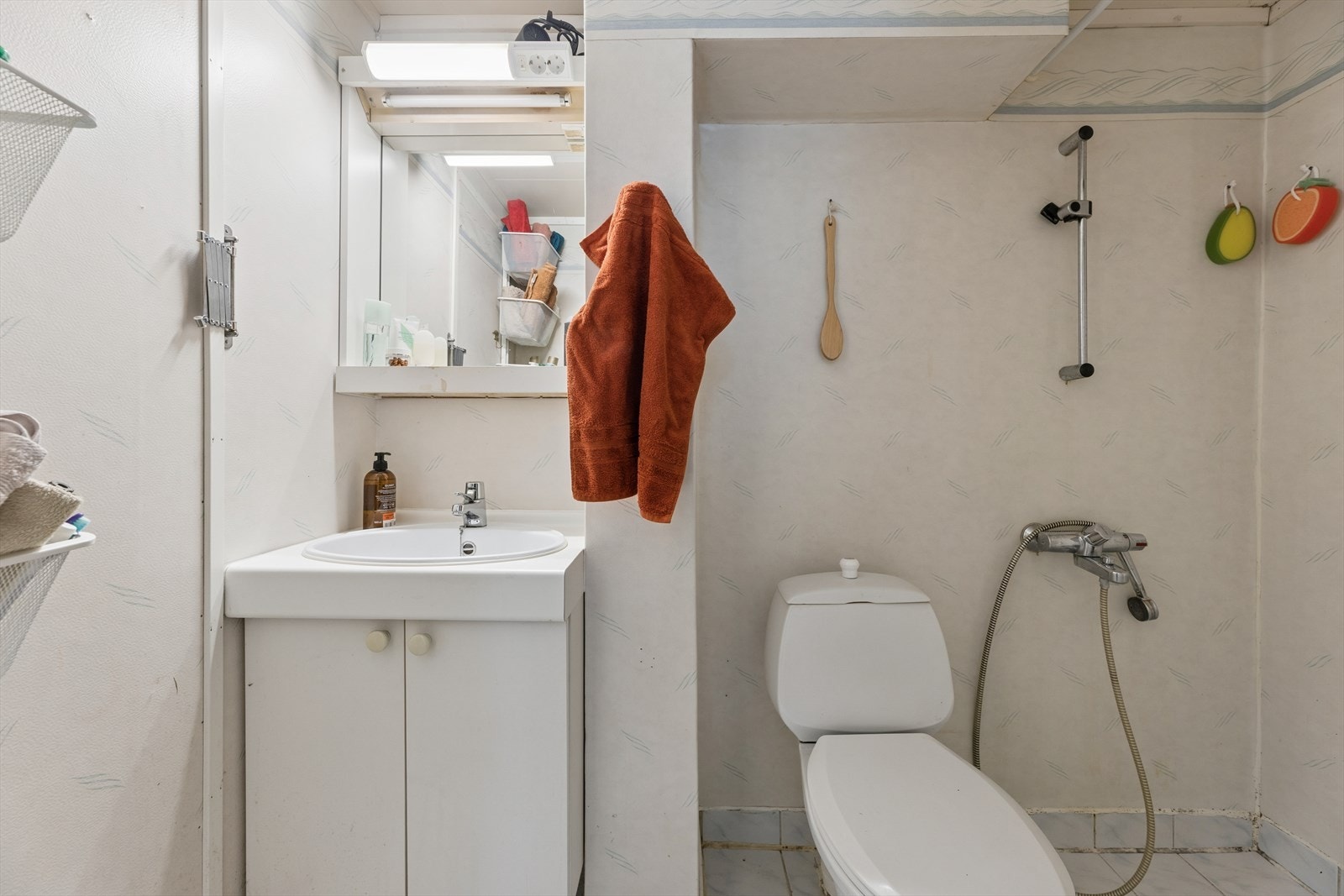 Badet består av gulvmontert toalett, åpen dusjsone med dusjgarnityr på vegg og innredning med servant. Galleribilde