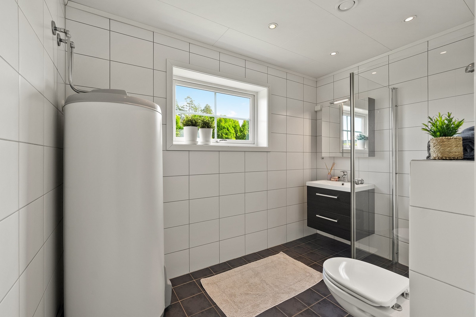 Badet har vegghengt servantinnredning med ovenpåliggende servant, speilskap med belysning, vegghengt toalett, og dusj på gulv med innfellbare dører av glass og metall, Galleribilde