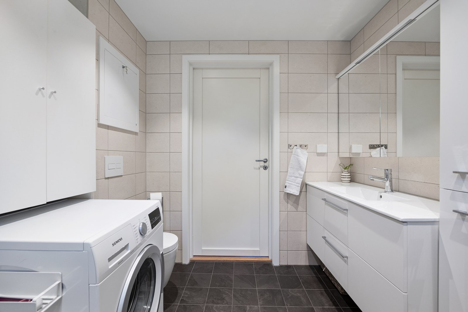 Badet er innredet med servantskap med ett-greps blandebatteri, speilskap, høyskap, vegghengt toalett med innebygget sisterne, avskjermet dusjhjørne med glass, blandebatteri og dusjgarnityr. Galleribilde