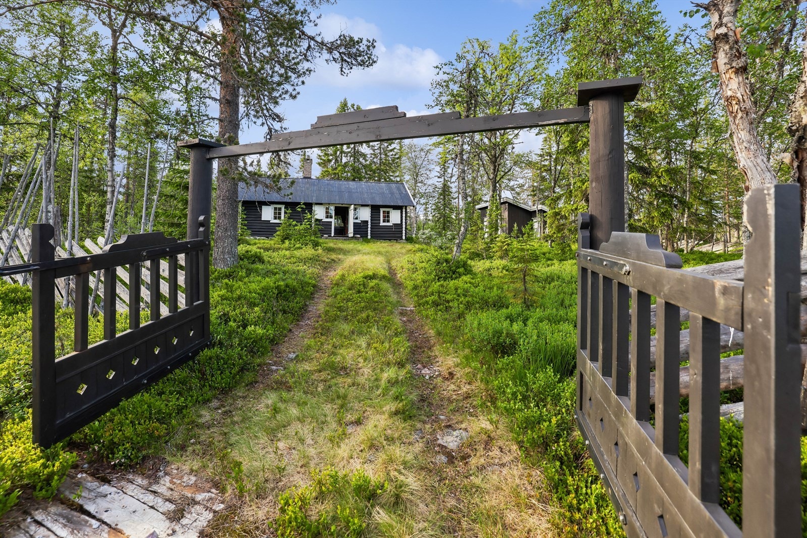 Adkomst inn gjennom grind og naturlig tunvei opp mot hytta. Galleribilde