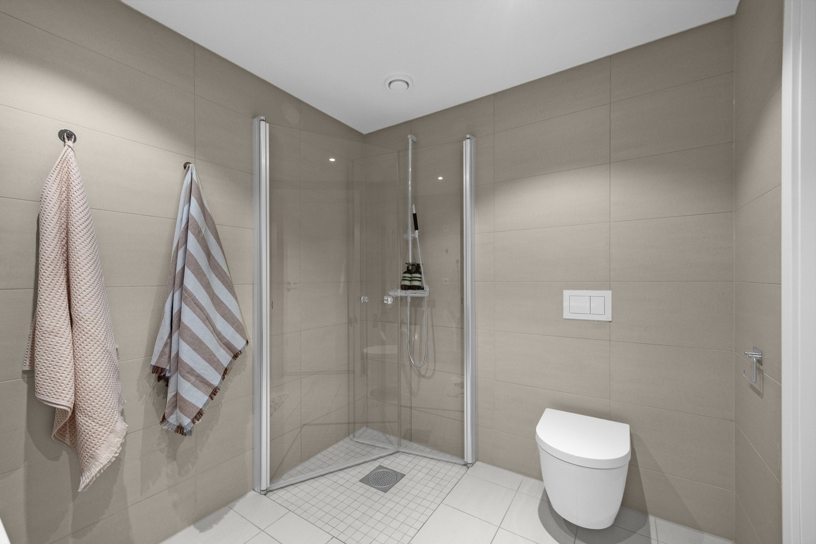 Badet har dusj og vegghengt toalett i nøytrale toner, lettstelt i hverdagen. Galleribilde
