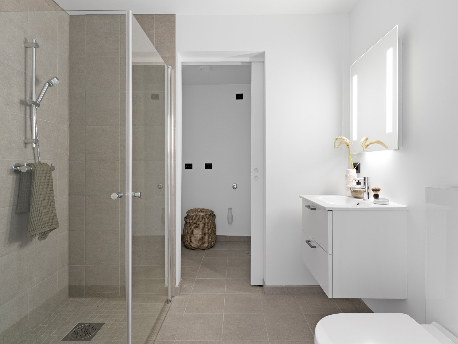 Leilighetens første bad har flislagt gulv og vegger i dusjsonen.I direkte tilknytning til badet ligger vaskerommet. Galleribilde