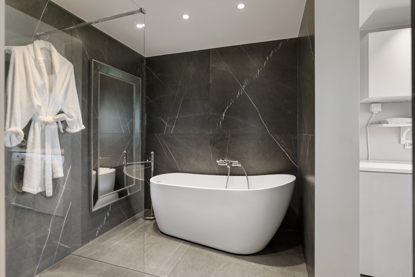 Badet byr på en innbydende kombinasjon av dusjnisje, badekar og eksklusive overflater - et rom skapt for både komfort og velvære. Galleribilde