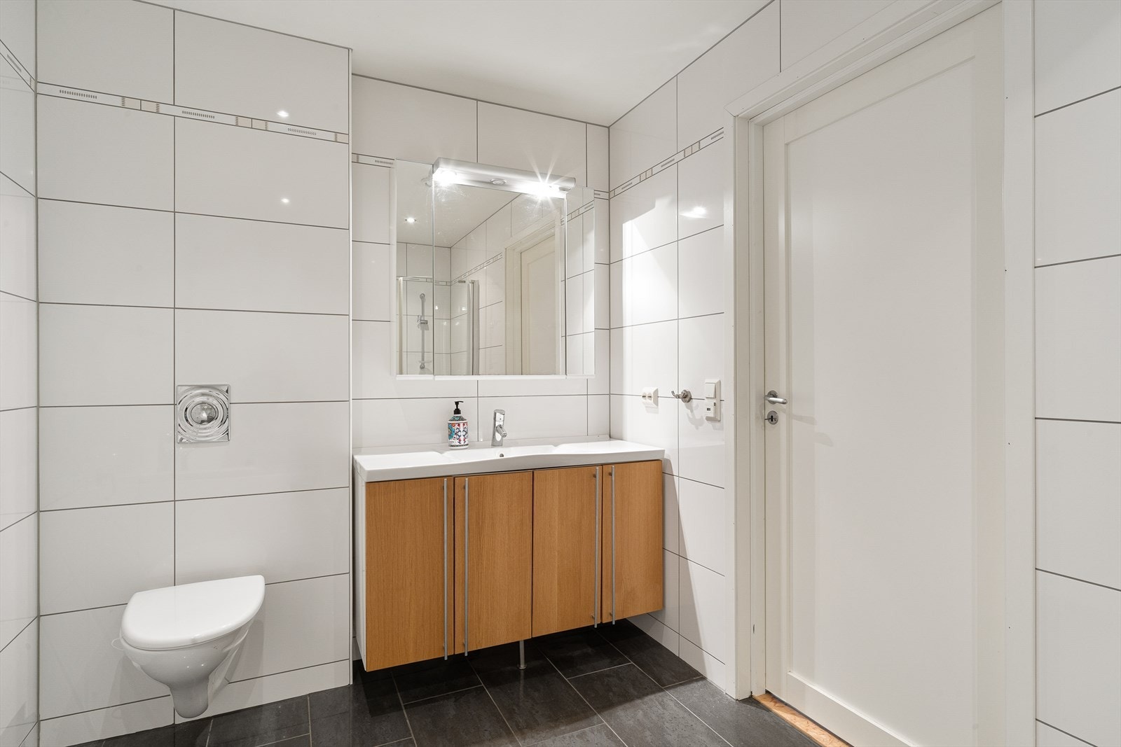Badet i kjelleren er helfliset med varmekabler på gulv og er innredet servant, vegghengt toalett, badekar og buede glassdører i dusj. Galleribilde