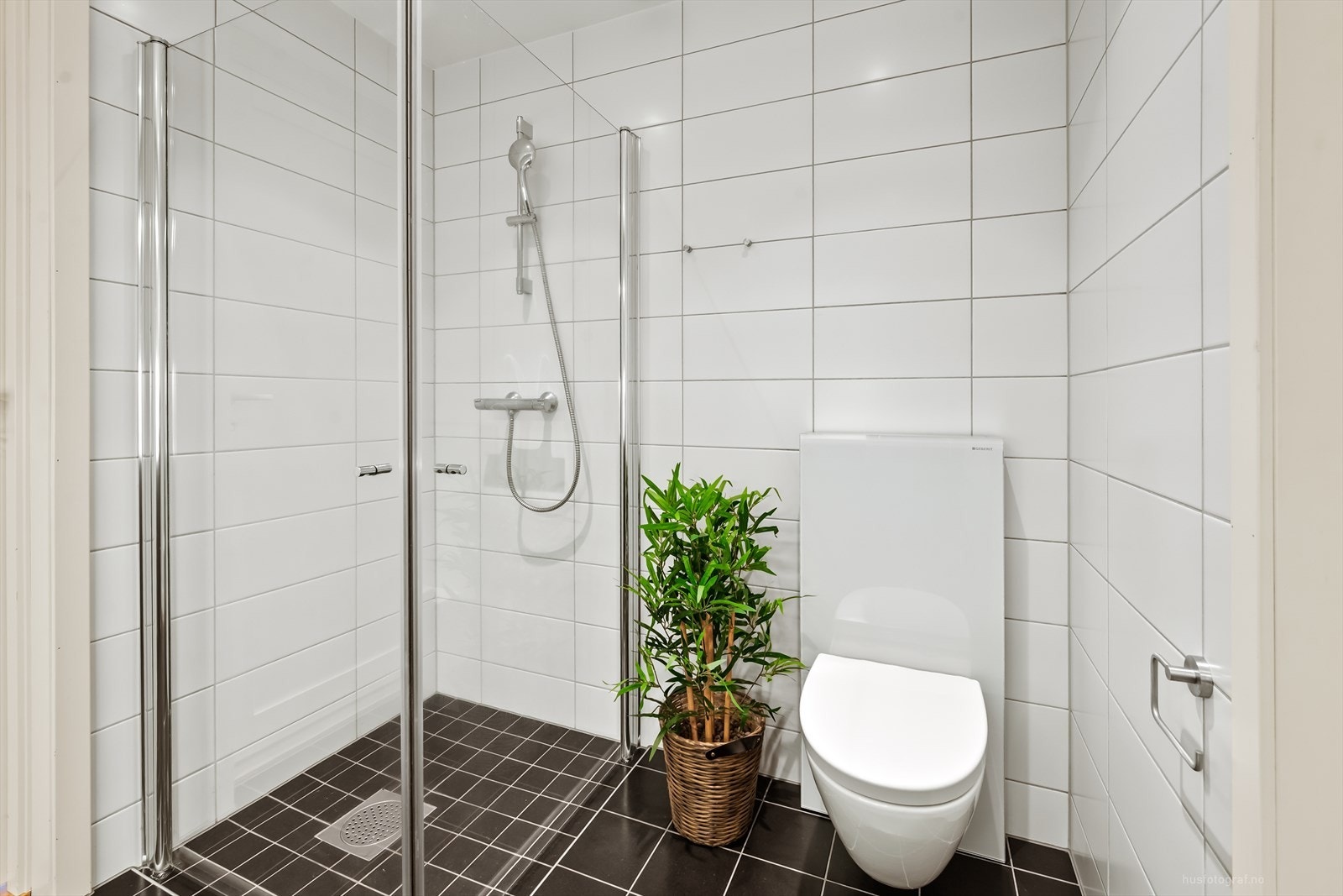 Badet er helfliset og har veggmontert toalett og dusjhjørne med innfellbare dører. Galleribilde
