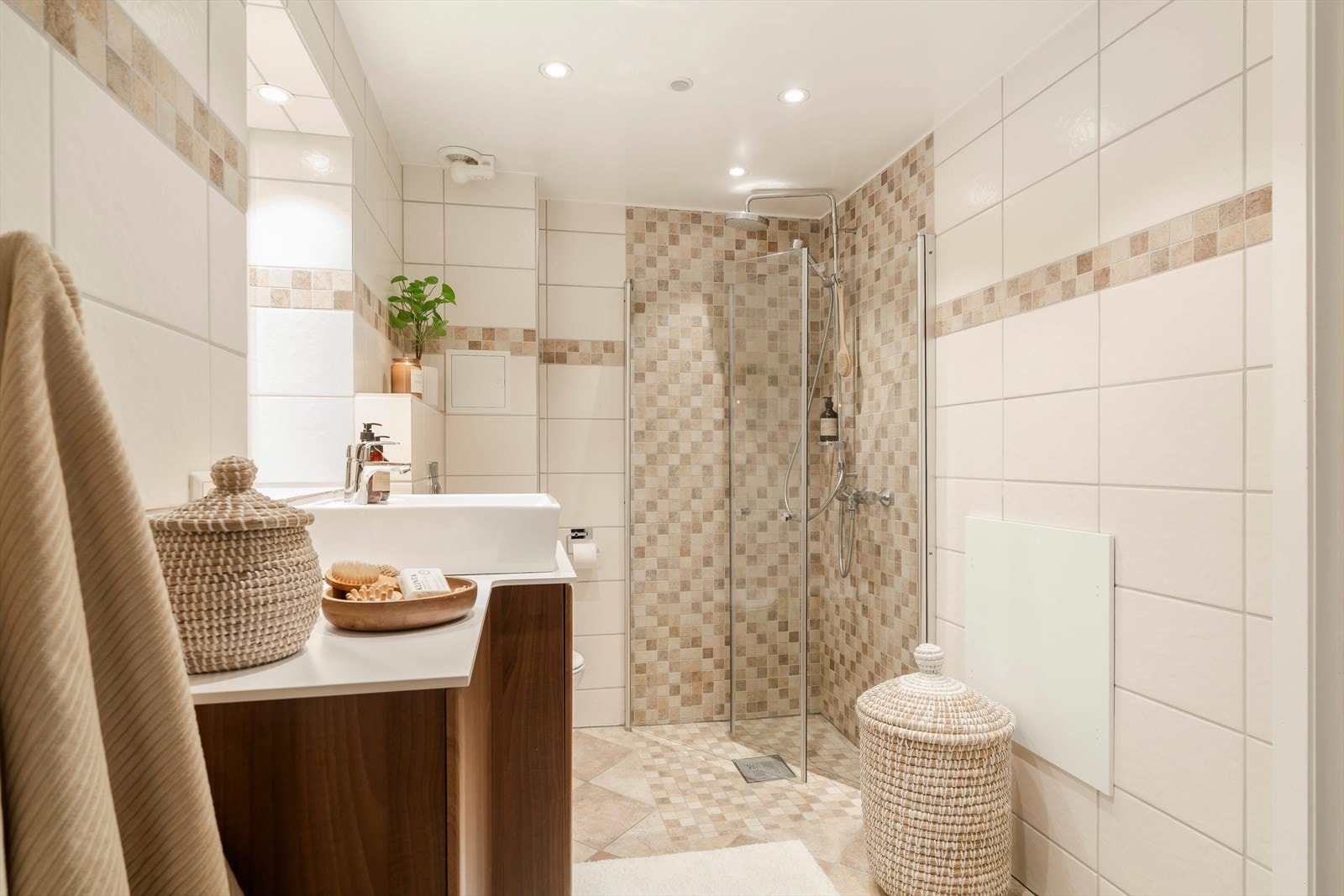 Badet er på ca. 5 kvm og har en praktisk og arealeffektiv utforming. Rommet er flislagt på vegger og gulv, og har innredning med servantskap, veggmontert toalett og dusjsone med innfellbare dusjvegger. Galleribilde