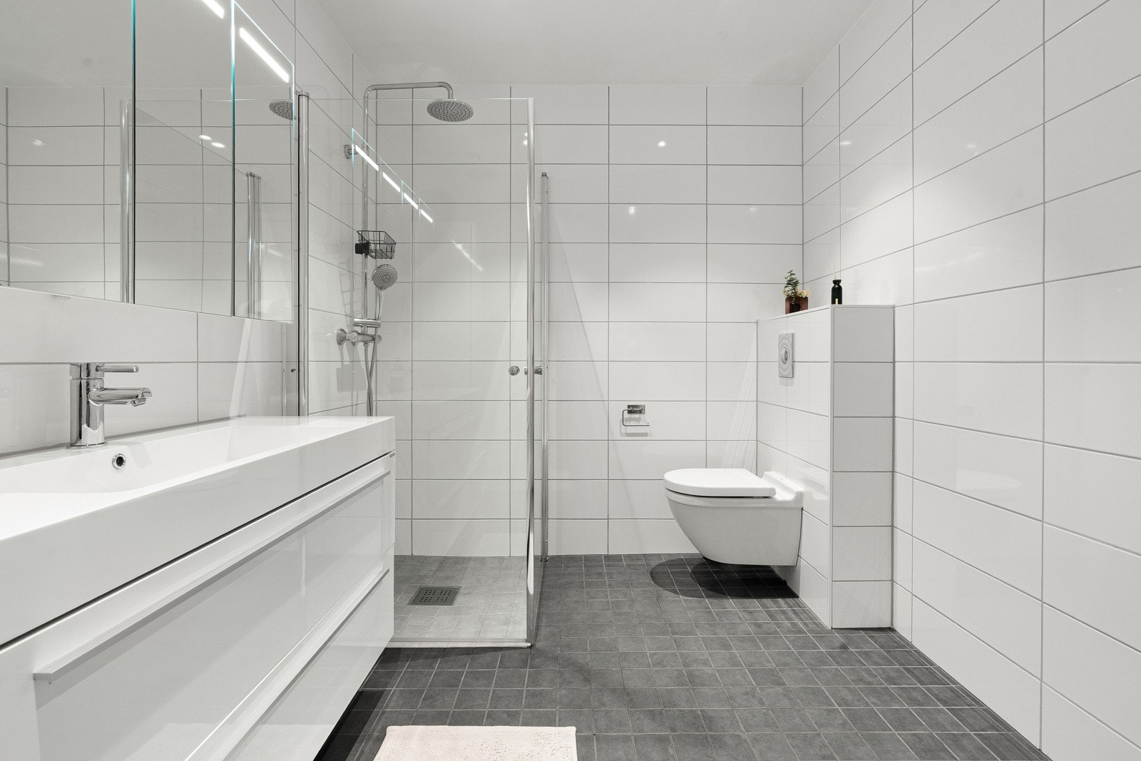 Delikat bad med fliser på gulv og vegger. Badet har gulvvarme, romslig dusjhjørne og et praktisk vegghengt toalett.