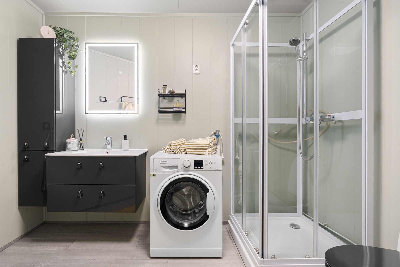 Badet er utstyrt med vegghengt servant, dusjkabinett, skap og opplegg for vaskemaskin.