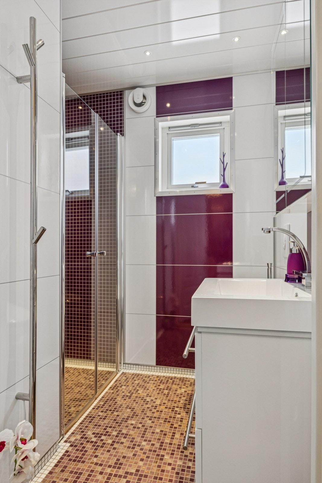 Flislagte vegger og gulv med mosaikkfliser gir badet et moderne preg. Elektrisk styrt vifte sørger for effektiv ventilasjon. Galleribilde