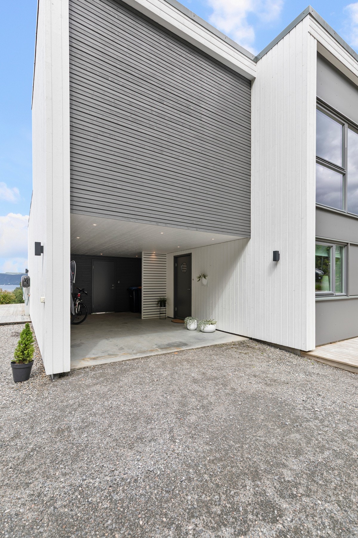 Praktisk carport med tilhørende bod på 12 kvm i bakkant, like utenfor inngangsdøren. Carporten har montert elbil-lader. Galleribilde