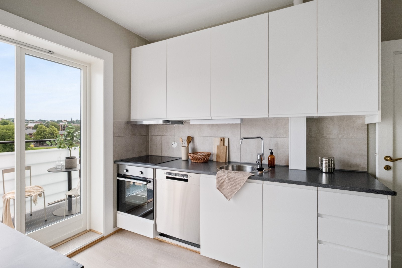 Tidsriktig glatt kjøkkeninnredning fra IKEA med soft close, fliser over benk, armatur, laminat benkeplate med nedfelt stålkum og keramisk topp. Galleribilde