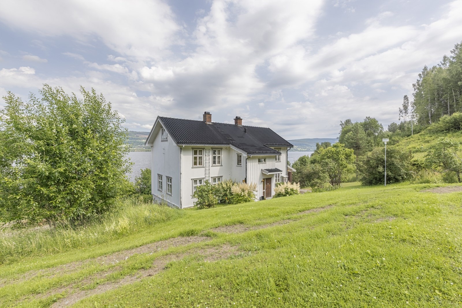 Oversiktsbilde av boligen med tilhørende hageanlegg. Den romslige tomten byr på flotte uteområder, frodig vegetasjon og en harmonisk innramming av den ærverdige eiendommen. Foto: GMP Galleribilde