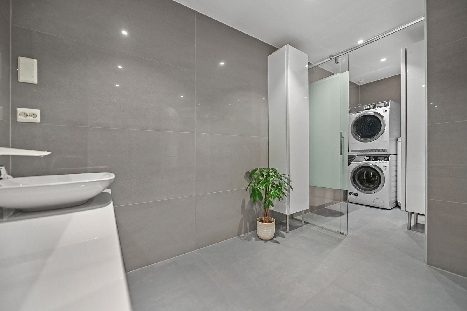 Bak en skyvedør av glass har badet en separat vaskeromsdel med utslagsvask, varmtvannstank og opplegg for vaskemaskin. Galleribilde