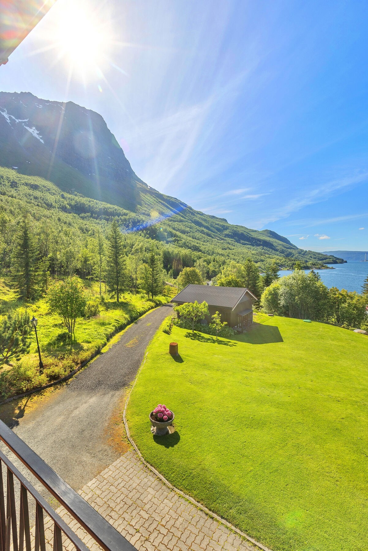 Utsikt fra verandaen ned mot den pent opparbeidede hagen og innkjørselen. Galleribilde