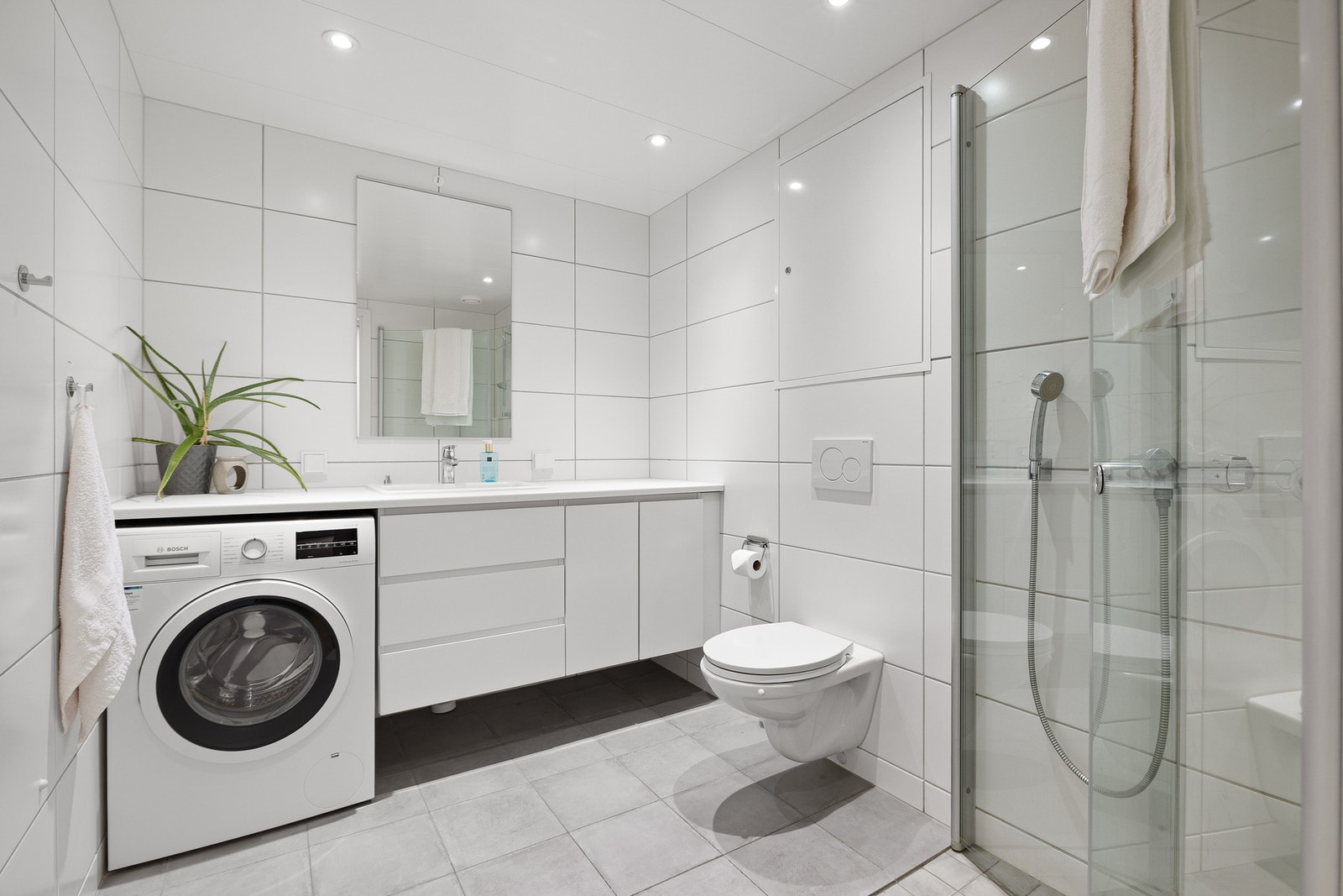 Leilighetens bad er pent flislagt og måler 4,9 kvm. Badet er utstyrt med innfellbare dusjdører i glass, varme i gulv og opplegg til vaskemaskin. Galleribilde